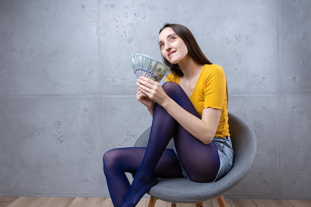 Photo of a wealthy woman in simple clothes holding a fan of dollar money isolated against a concrete wall background