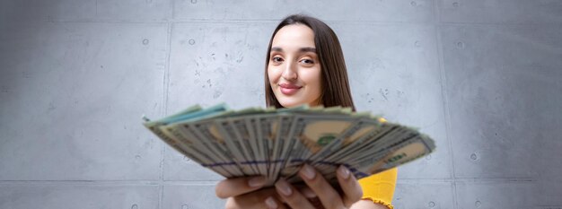 Photo of a wealthy woman in simple clothes holding a fan of dollar money isolated against a concrete wall background