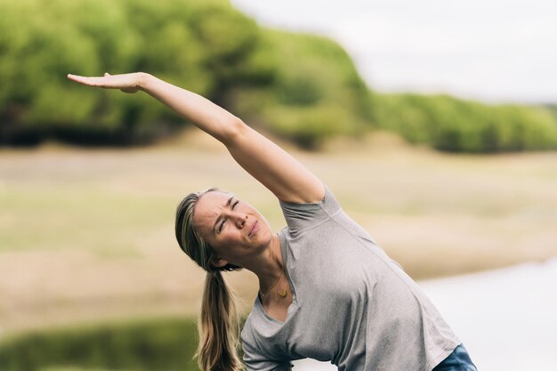 Foto con copia spazio di una donna che allunga la schiena mentre alza il braccio facendo yoga in un parco