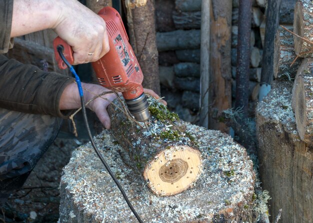 Foto foto con blocchi di legno mano umana che tiene un trapano che fa buchi in un tronco di legno