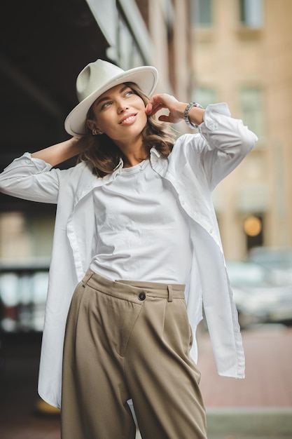 Photo of a woman in a hat poses on street against buildings