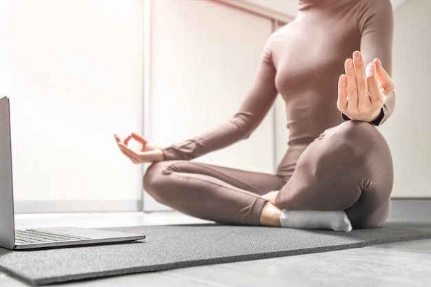 Photo of woman practicing yoga training online at home with laptop.