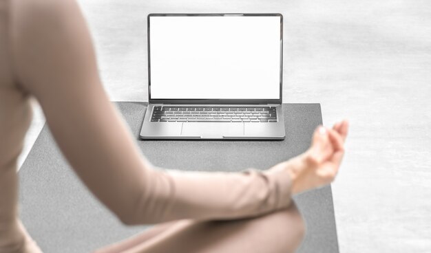 Photo of woman practicing yoga training online at home with laptop.