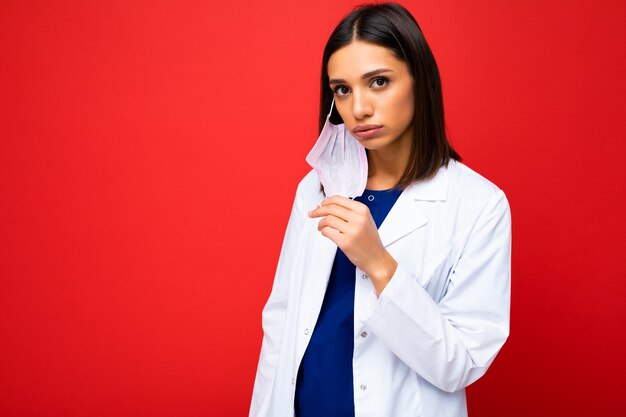 Photo of woman taking off virus protective mask on face against coronavirus and white medical coat