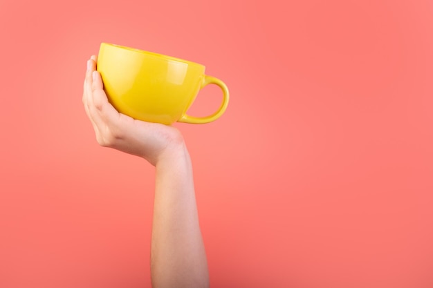 Foto foto di una tazza di caffè gialla in mano isolata su sfondo rosa design banner tazza di tè