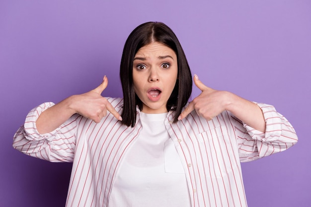 Photo of young astonished woman indicate fingers herself offended puzzled isolated over violet color background