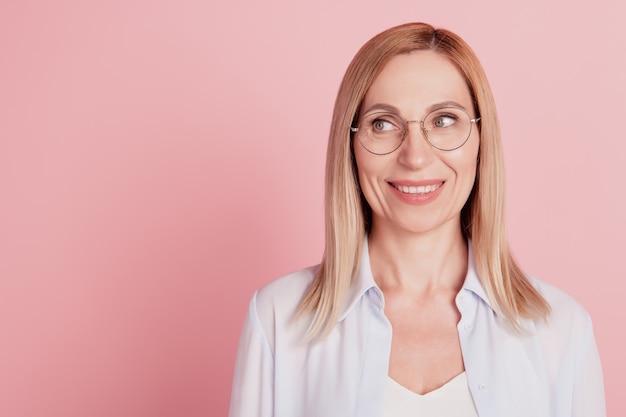 Photo of young attractive woman happy positive smile look empty space wear glasses isolated over pink color background