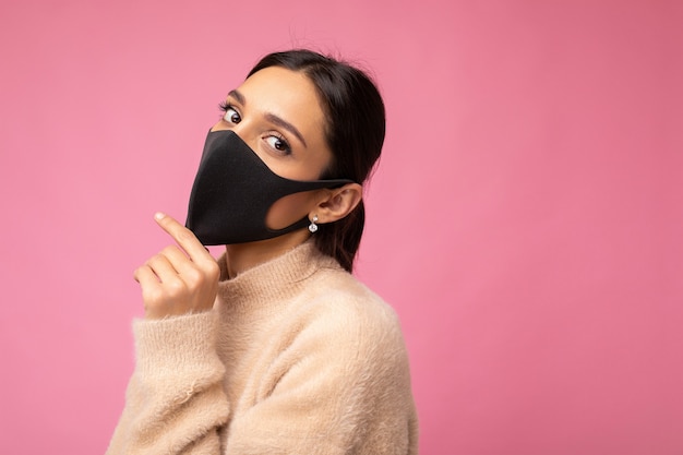 カラフルな背景の壁に分離された手作りの綿生地のフェイスマスクを身に着けている若い魅力的な女性の写真。 COVID-19に対する保護。