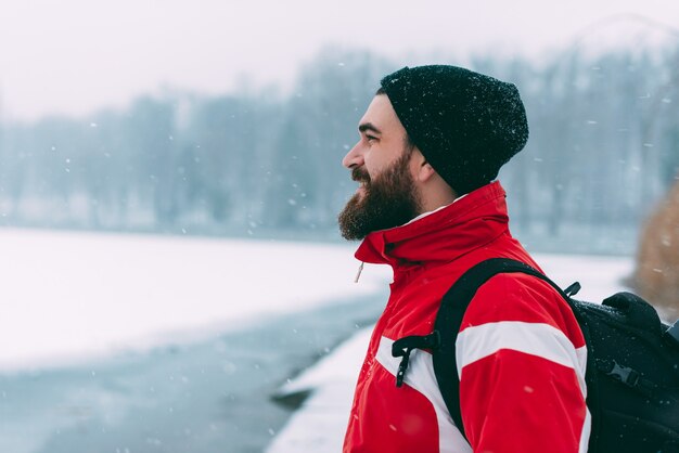 Photo of a young bearded man looking and smiling at a frozen lake in a winter season