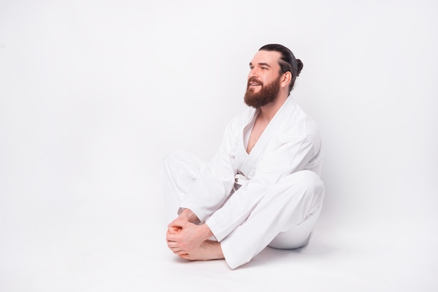 Photo of young bearded man wearing taekwondo uniform making stretching butterfly  pose