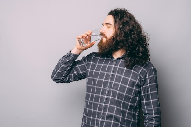 Photo of young bearded man with long hair drinking glass of fresh water