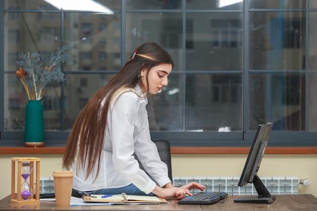 The photo of a young beautiful lady sitting at the office and working on pc