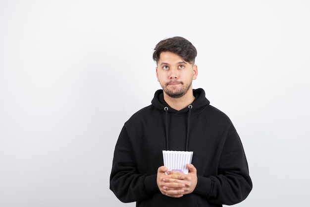 Photo of young beautiful man watching television series and holding popcorn bucket 