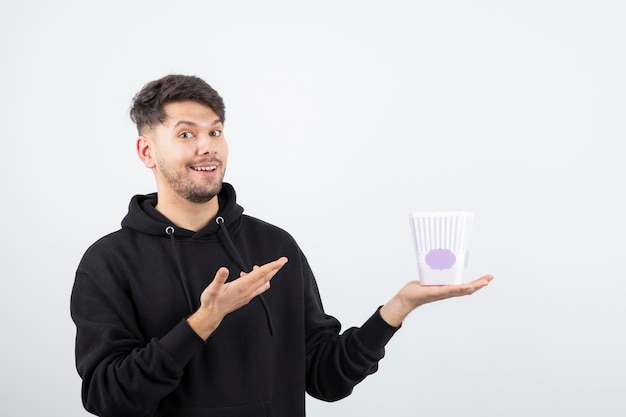 Photo of young beautiful man watching television series and holding popcorn bucket 