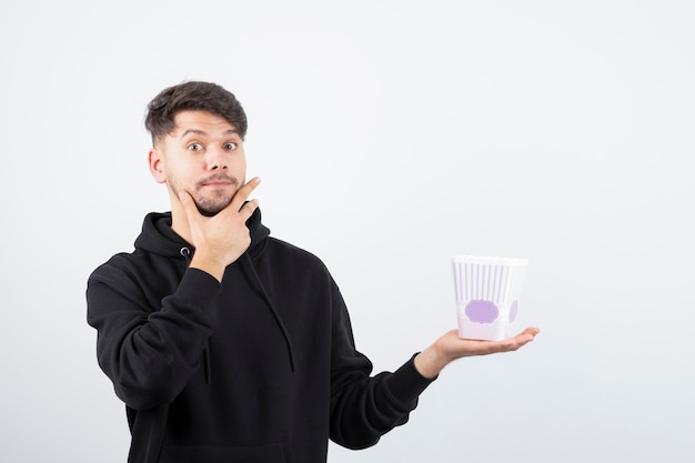 Photo photo of young beautiful man watching television series and holding popcorn bucket