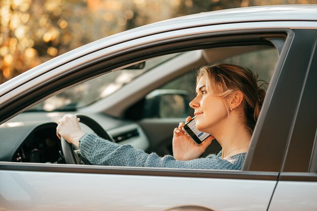 Фотография молодой красивой женщины, которая ведет машину, нарушает правила дорожного движения, отвлекается, смотрит на экран