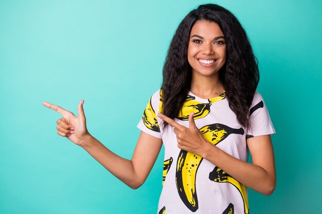 Photo of young black girl direct fingers empty space wear banana print t-shirt isolated teal color background