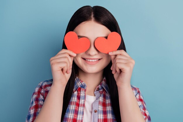 Фото молодой веселой девушки прикрывают глаза сердце романтический день святого валентина, изолированные на бирюзовом цветном фоне