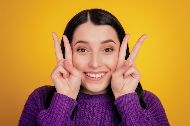 Photo of young cheerful girl happy positive smile show v-sign peace cool isolated over yellow color background