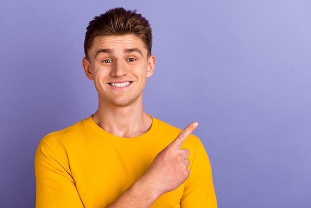 Photo of young cheerful guy indicate finger empty space promo recommend isolated over violet color background