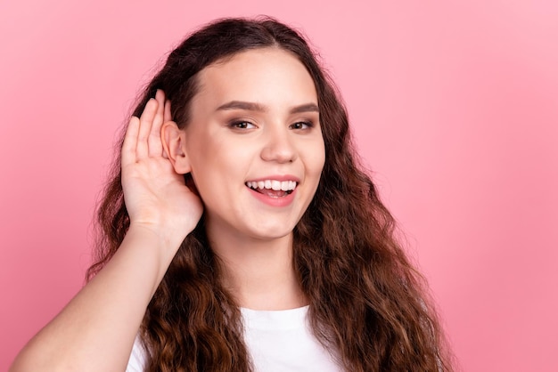 Photo of young cheerful lovely girl arm near ear listen news eavesdrop isolated over pink color background.