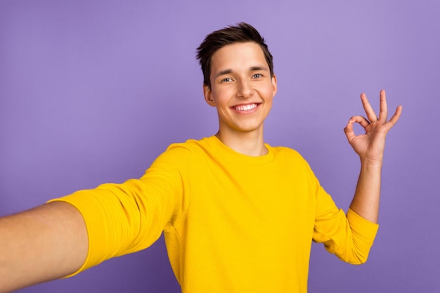Photo of young cheerful man make okay symbol choice advice take selfie isolated over bright color background
