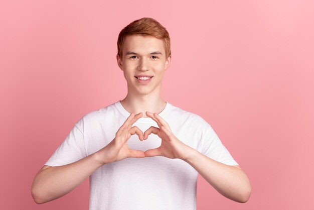La foto del giovane uomo allegro mostra le dita cuore sybol amore sentimenti cupido isolati su sfondo di colore rosa