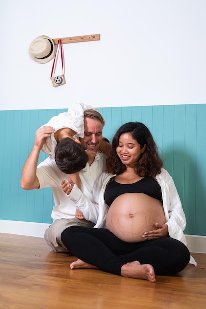 Photo of young cheerful positive smiling couple pregnant wife and husband with their son relaxing at home