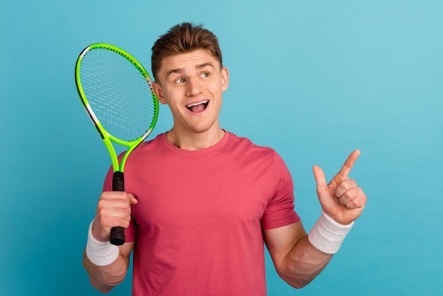 Photo of young excited man look indicate finger empty space promo suggest play tennis sporty isolated over blue color background