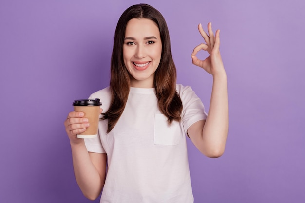 Photo of young girl enjoy cup of coffee show oakey perfect choose sign isolated over violet color background