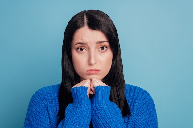 Фотография руки молодой девушки касаются подбородка несчастной грустной расстроенной обиженной подчеркнутой депрессивной неудачей, изолированной на синем цветном фоне