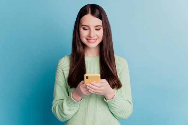 Photo of young girl typing message smartphone isolated on blue background