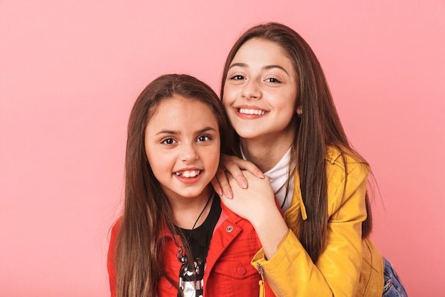 Photo of young girls in casual hugging together, isolated over red wall