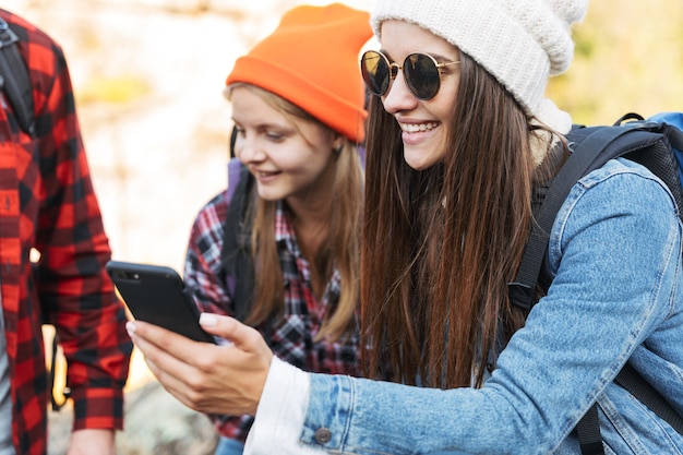 Photo of young group of friends outside in free alternative vacation camping over mountains using mobile phone, focus on girl.