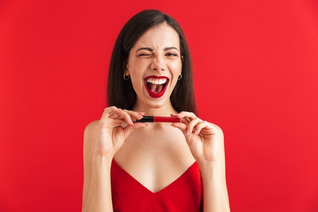 Photo of young happy excited woman posing isolated holding lip gloss doing makeup.