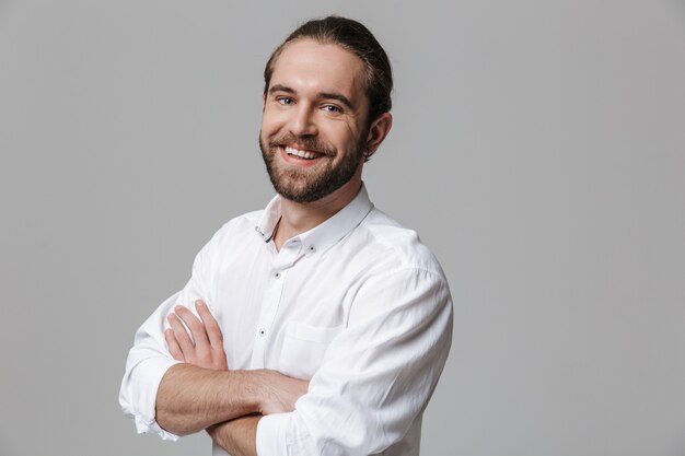 Photo of a young happy optimistic handsome bearded man posing isolated over grey wall.