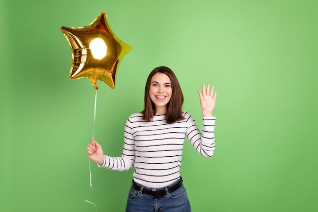 Photo of young lovely woman hold air ball decor inflate waving arm hi isolated over green color background.