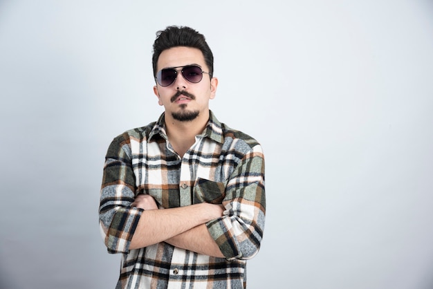 Photo of young man in black glasses standing on white wall.