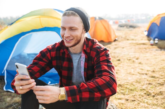 Photo of young man outside in free alternative vacation camping over mountains using mobile phone chatting.