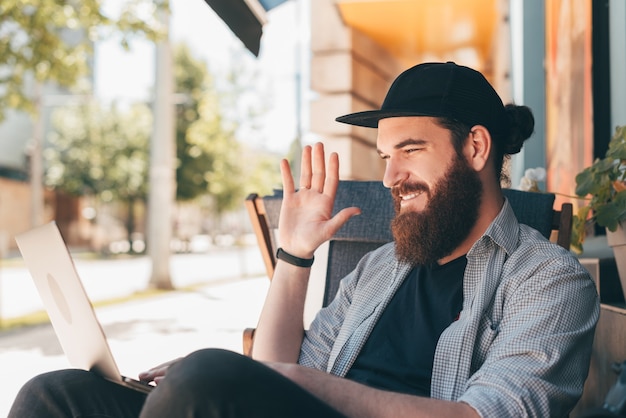 Photo photo of young man with beard freelancer sitting and talking on web camera with client