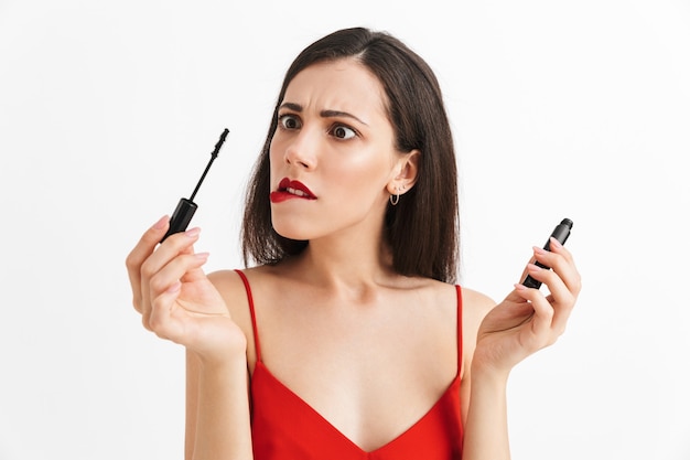 Photo of young nervous beautiful woman posing isolated holding lip gloss doing makeup.