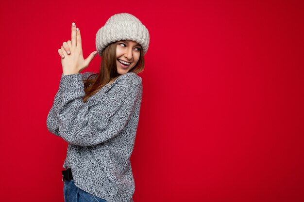 Photo of young positive happy smiling beautiful woman with sincere emotions wearing stylish clothes isolated over background with copy space and showing gun gesture