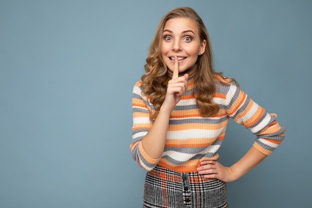 Photo of young positive happy smiling beautiful woman with sincere emotions wearing stylish clothes isolated over wall with copy space and showing shhh gesture.