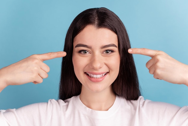 Photo of young pretty girl indicate fingers eyes oculist vision healthy isolated over blue color background.