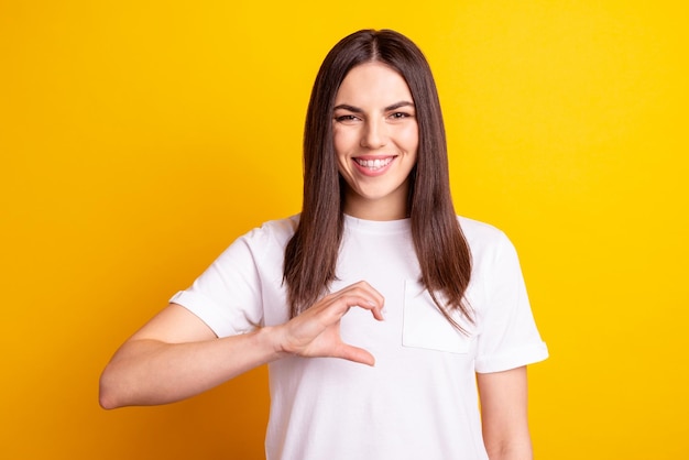 La foto di una giovane ragazza carina mostra la metà delle dita dei sentimenti di cupido del cuore isolati su uno sfondo di colore giallo