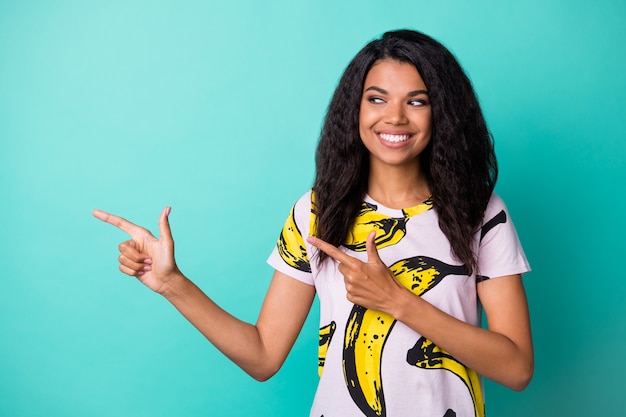 Photo of young pretty girl toothy smile direct finger interested look empty space wear banana print t-shirt isolated teal color background