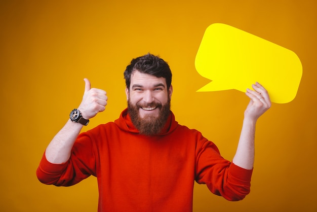 Photo of young smiling guy is holding a bubble speech and thumb up or like gesture.