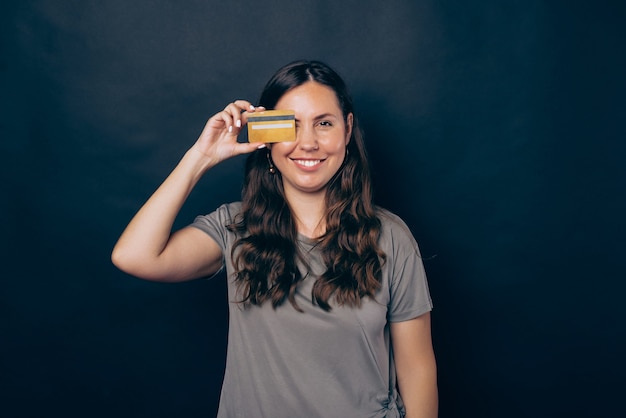 Photo of young smiling woman covering eye with yellow credit card