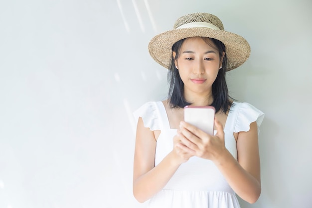 흰 드레스와 밀짚 모자를 쓴 행복한 젊은 여성의 사진 긍정적인 미소는 스마트폰을 사용하여 사회 기술 여행 휴식의 개념