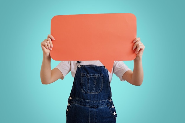 Photo young woman holding speech balloon orange poster covering her face isolated on blue background